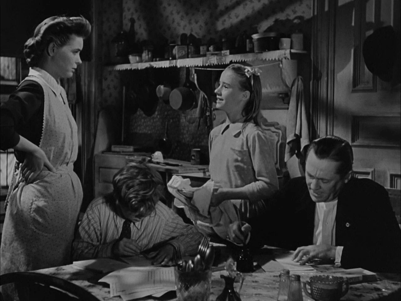 A Tree Grows In Brooklyn (1945) movie still: medium — A dimly lit room with shelves containing miscellaneous items in the background. Three people…