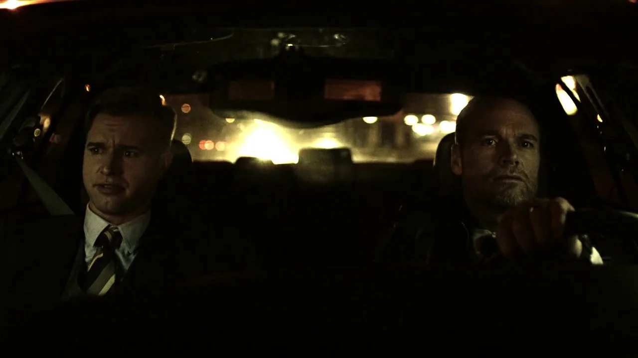 Hellraiser: Judgement (2018) movie still: medium — The interior of a moving car at night with two men in the front seats. Bright headlights and…