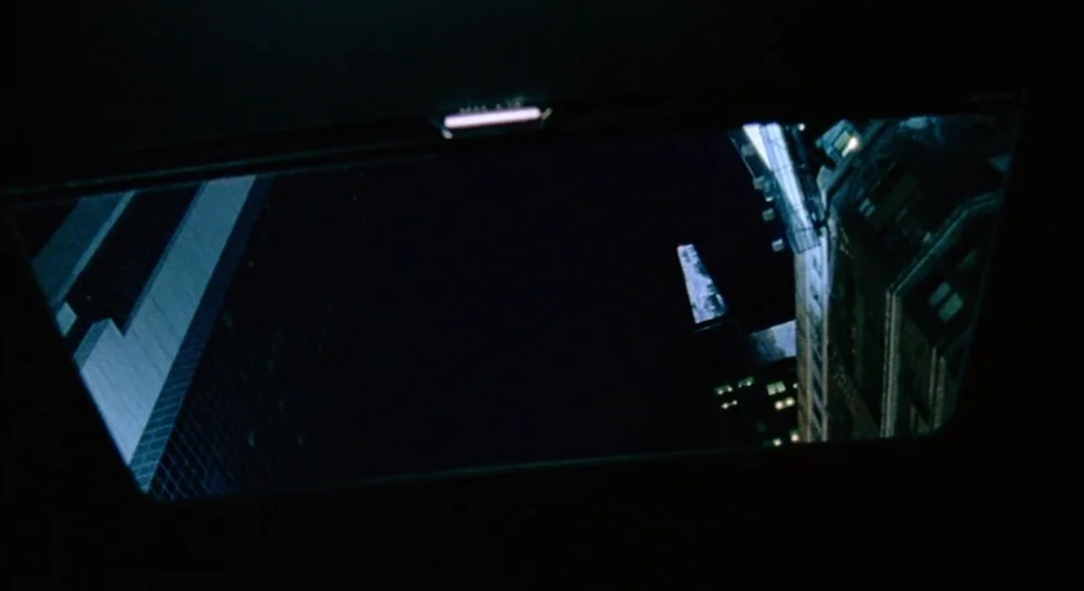 Hamlet (2000) movie still: establishing — A view of city skyscrapers at night from inside a vehicle sunroof. The dark sky fills the center while…