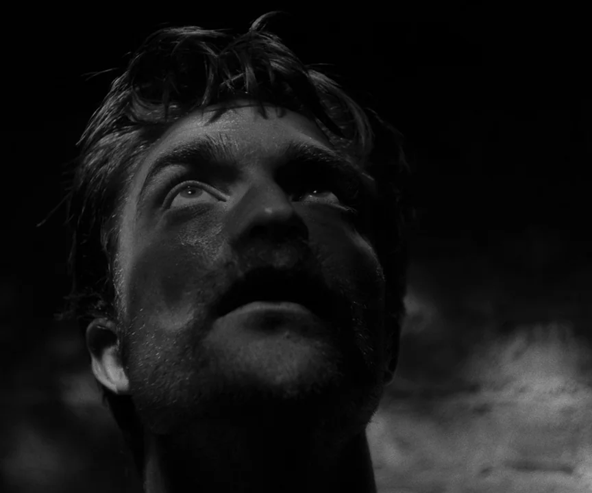 The Lighthouse (2019) movie still: closeup — A dark, cramped lighthouse interior illuminated by a harsh light source from below. A man with…