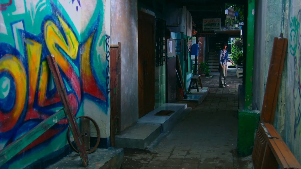 Merantau (2009) movie still: wide — A narrow paved path is enclosed by concrete walls covered in bright spray-painted murals. A single man stands in…