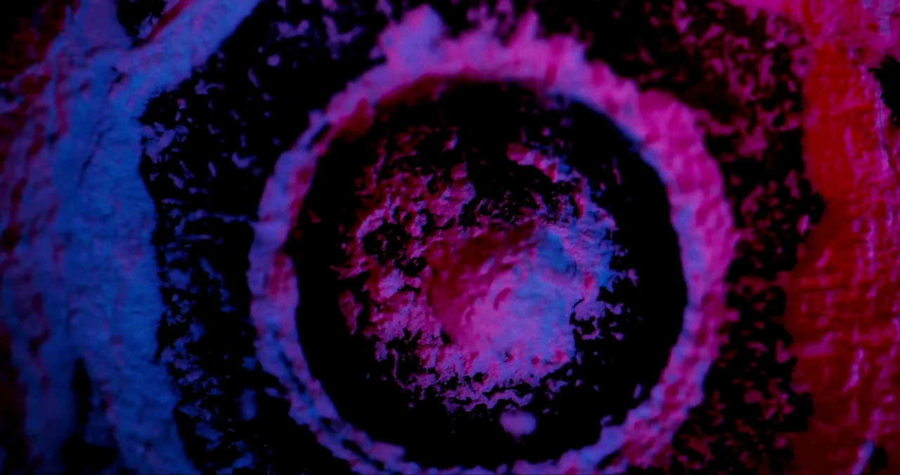 Violet (2021) (2021) movie still: closeup — An abstract circular texture appears with rough particulate surfaces and concentric rings. The frame is…