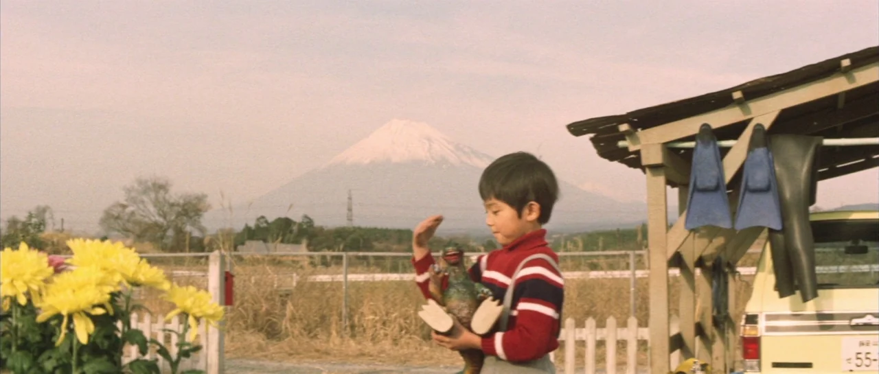 Godzilla Vs Hedorah (1971) movie still: medium — A Japanese child stands in a rural landscape near a simple wooden shelter structure. Mount Fuji…