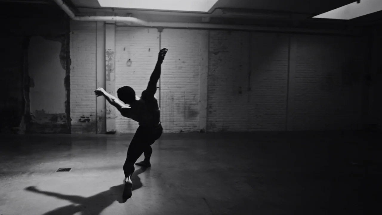 Kokomo City (2023) movie still: fullbody — A minimalist studio space features white painted brick walls and smooth concrete floors. A male dancer…