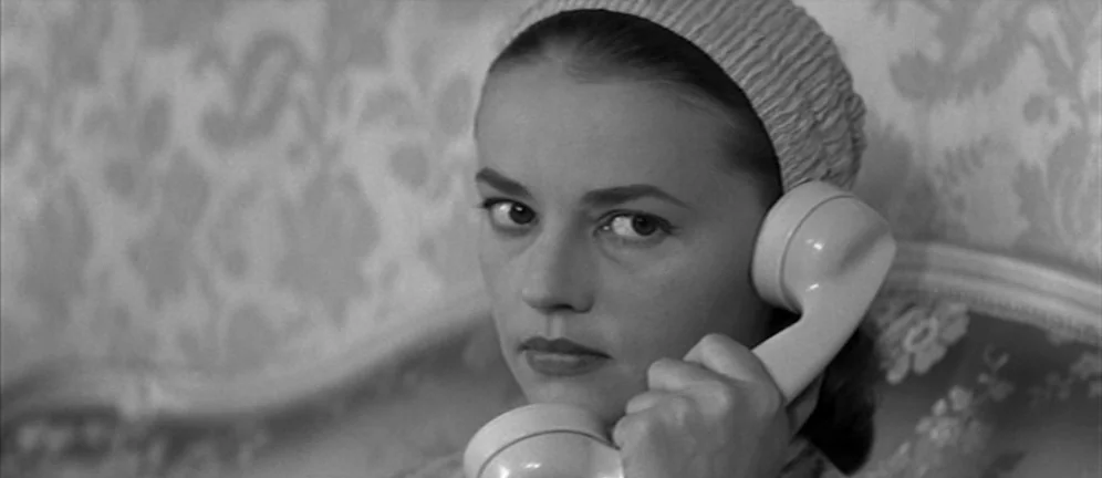 Les Amants (1958) movie still: closeup — A woman sits indoors against a wall with intricate floral wallpaper patterns. She holds a vintage telephone…