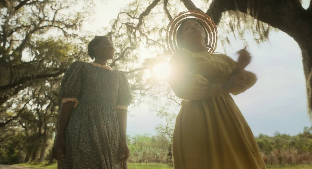 The Color Purple (2023) movie still: fullbody — A field filled with moss-draped trees under bright sky provides an outdoor setting. Two women stand…