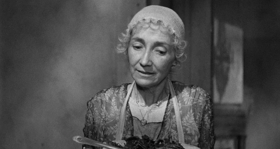 Baby Doll (1956) movie still: medium — An older woman stands in a dimly lit, shadowed room. She holds a plate of food while looking downward.