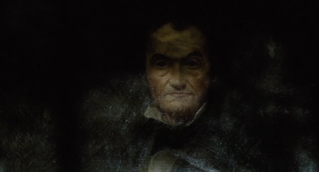 Foxcatcher (2014) movie still: closeup — A dimly lit, shadowed space obscures the background entirely. An elderly man with weathered features faces…