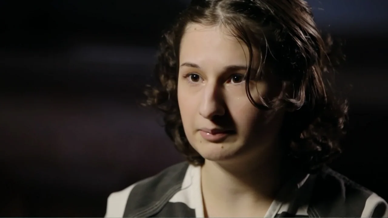 Mommy Dead and Dearest (2017) movie still: closeup — A dark interview space with an out-of-focus background. A young woman in a prison uniform looks…