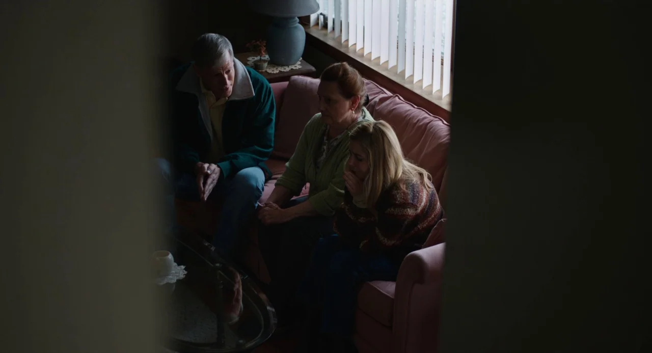 The Miseducation of Cameron Post (2018) movie still: medium — A dimly lit room with a pink sofa positioned against a window with blinds. Three…