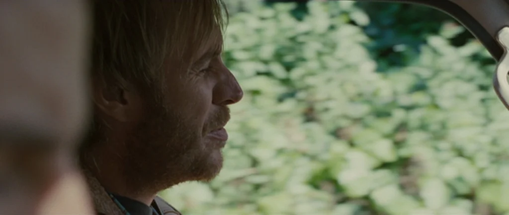 Greenberg (2010) movie still: closeup — A man sits in the driver seat of a moving car in daylight. The background outside the window is a blurred…