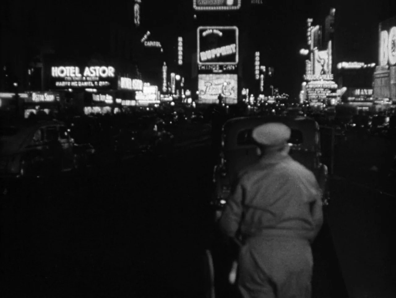 The Naked City (1948) movie still: medium — A dense urban night street is cluttered with tall glowing billboard signs and traffic. A person drives a…