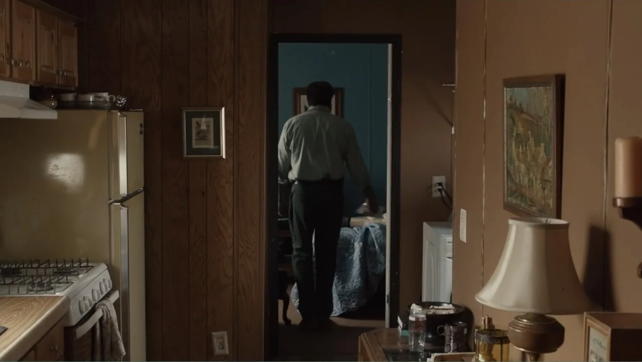 The Cleaner (2021) movie still: medium — A wood-paneled kitchen leads into a bedroom with blue walls and a bed. The man walks away from the kitchen…