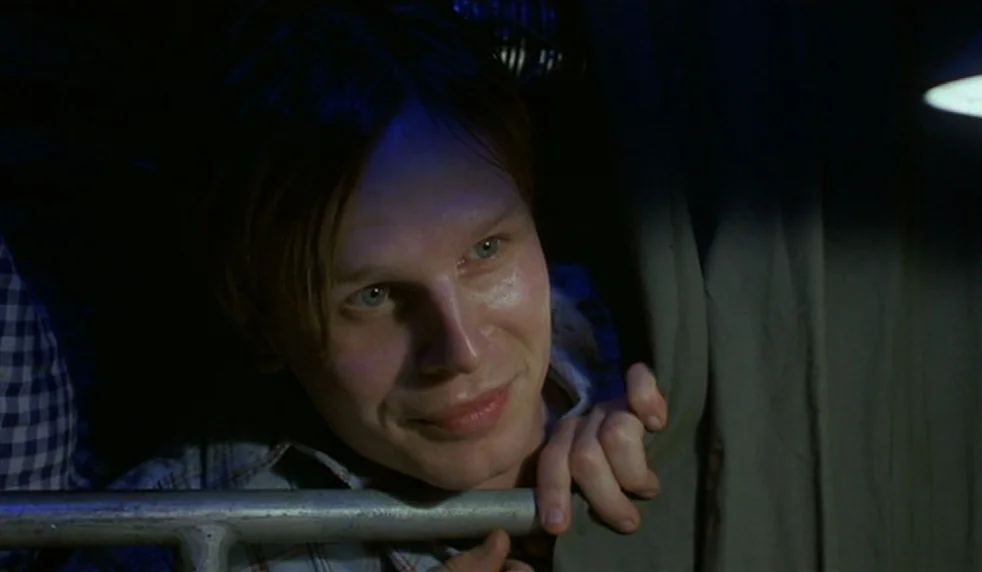 Das Boot (1981) movie still: closeup — A dimly lit cabin features gray fabric curtains and a metallic horizontal safety rail. A young man with light…