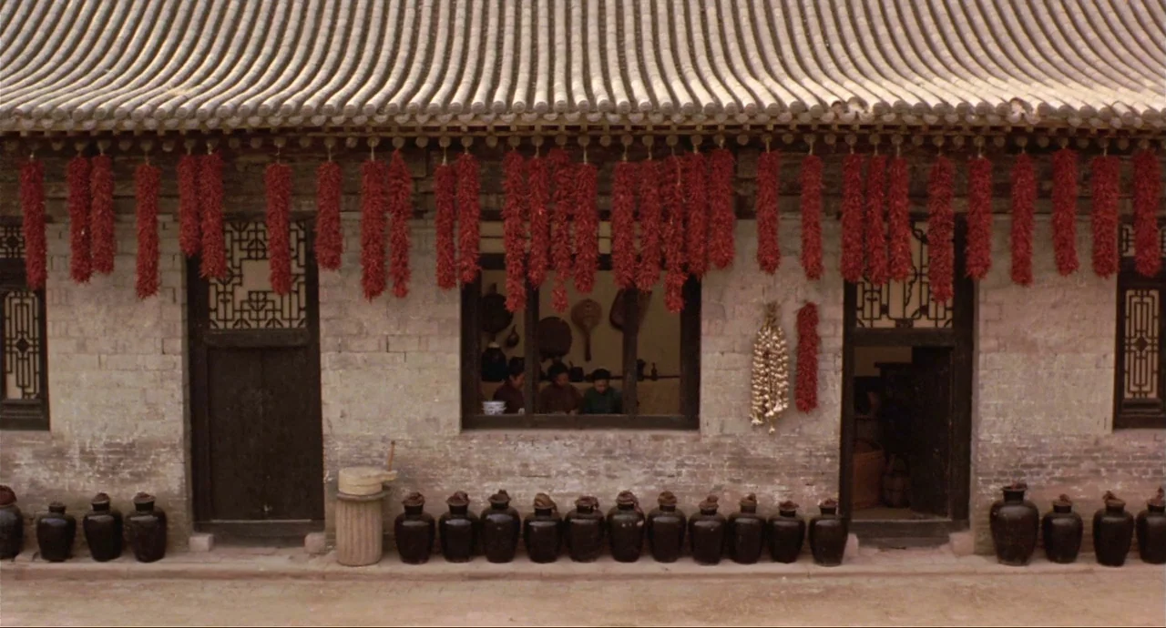 Raise The Red Lantern movie still: wide — A traditional stone building features symmetrical doorways and rows of dark ceramic storage jars. Numerous…