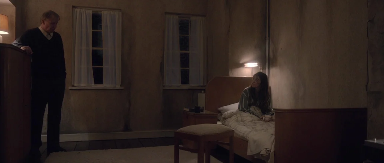 Nymphomaniac Vol 2 (2013) movie still: wide — A sparsely furnished room features two windows and a bed against a plain wall. A man stands at the…