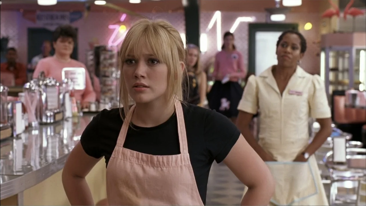 A Cinderella Story (2004) movie still: medium — A retro-style diner interior with chrome fixtures and neon decor signs on walls. A young blonde…