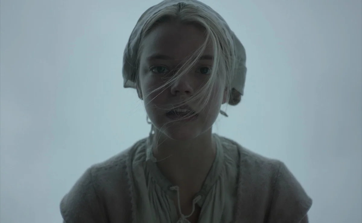 The Witch (2015) movie still: closeup — A pale, overcast outdoor setting provides a blank, featureless gray background. A young woman wears a…