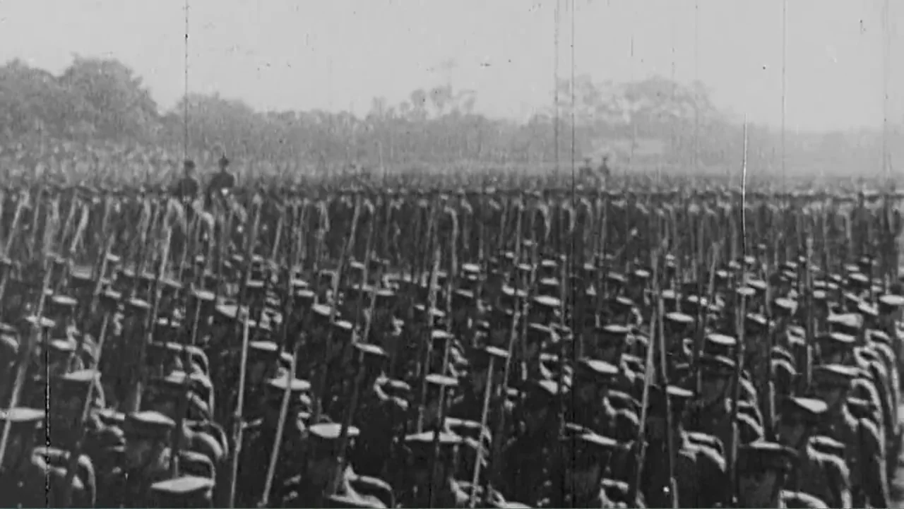 Finding Amelia (2024) movie still: wide — A vast, dense formation of soldiers stands on a flat outdoor expanse. The men hold vertical rifles while…