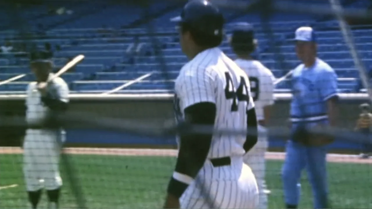 Reggie (2023) movie still: medium — A professional baseball field with empty blue stadium seating visible in the background. A player in a…
