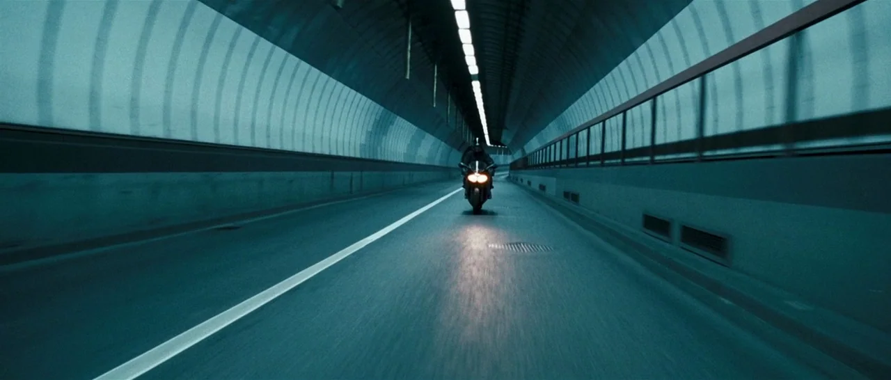Green Street (2005) movie still: wide — A long, curved concrete tunnel with rows of recessed ceiling lights and metal walls. A motorcyclist moves…