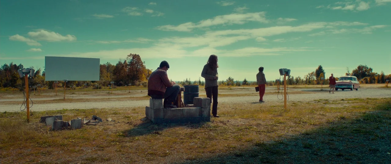 Scary Stories to Tell in the Dark (2019) movie still: wide — A vast, gravel-covered drive-in theater lot features a large, blank screen and speaker…