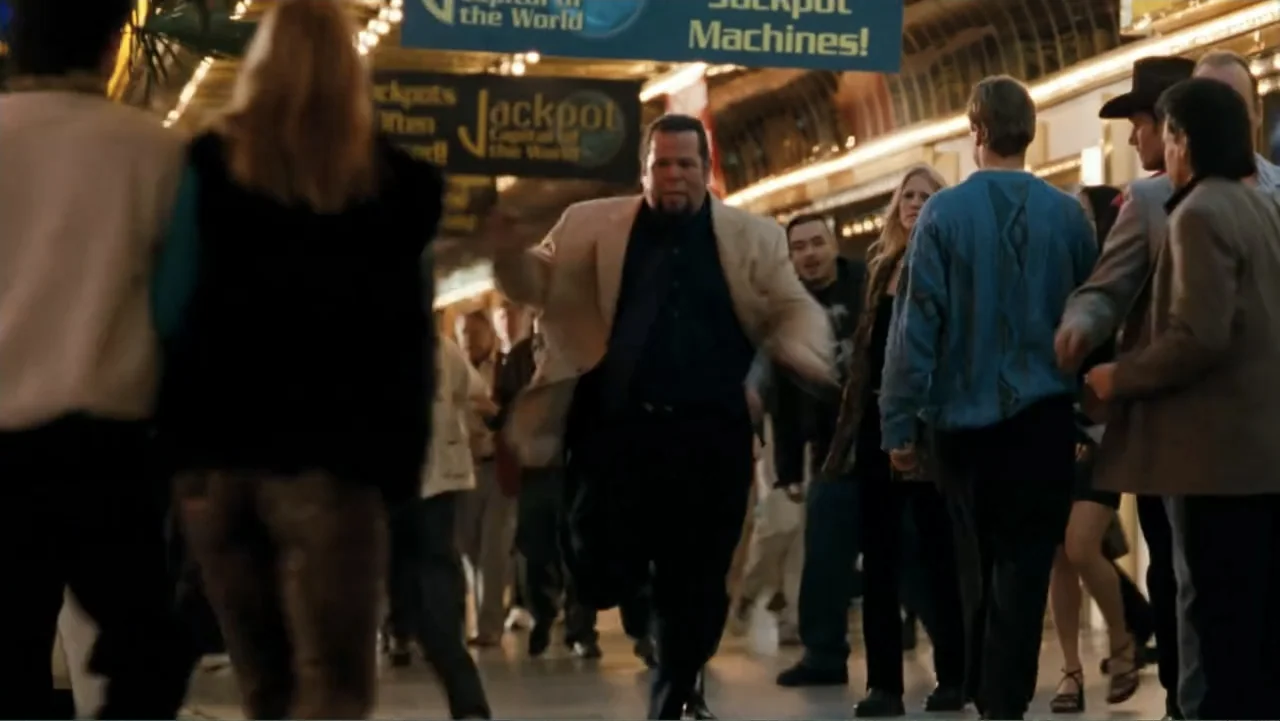 Get Carter (2000) movie still: medium — A bustling interior casino walkway with blue overhead advertising signs and moving crowds. A man in a light…