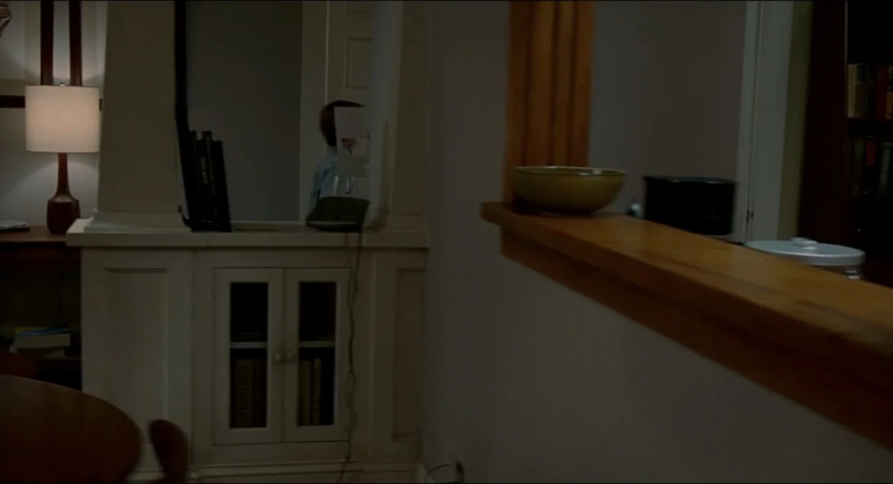 The Ring Two (2005) movie still: medium — A dimly lit indoor space featuring a wooden console table and a table lamp. A young child in a blue shirt…