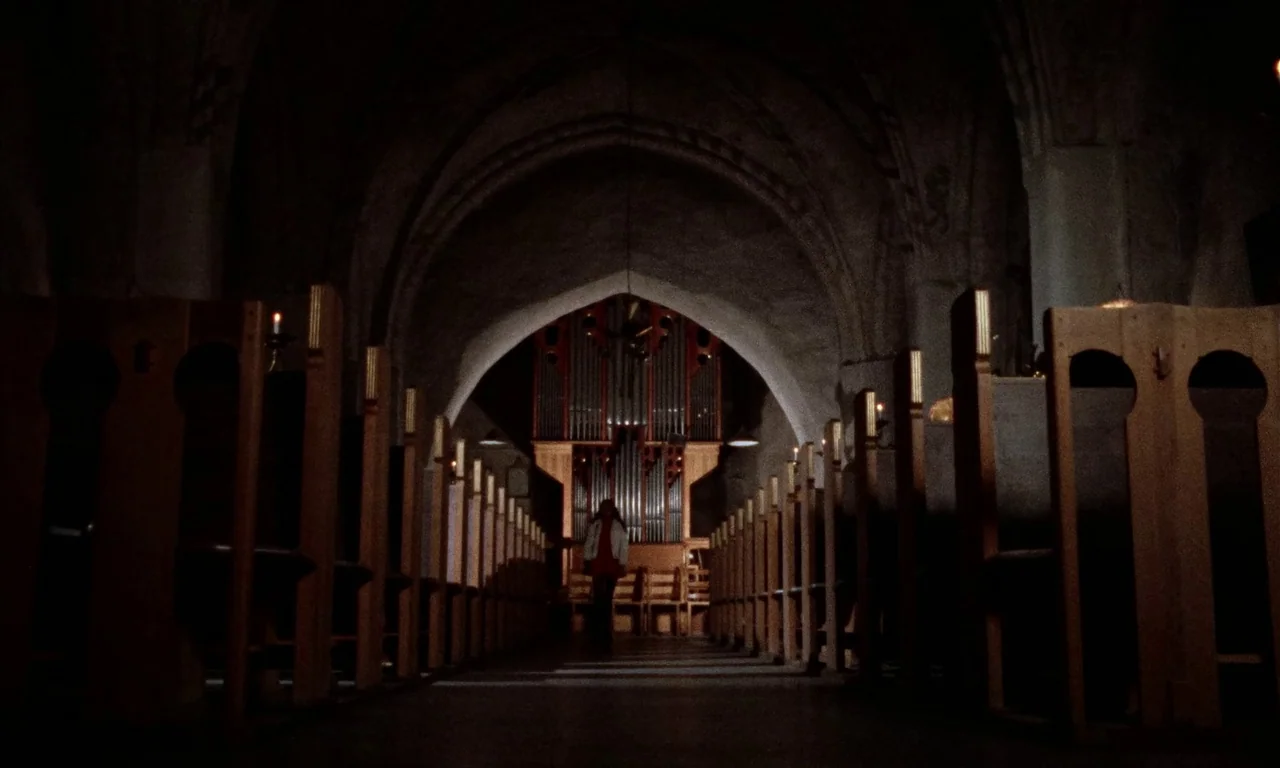 Thriller: A Cruel Picture (1973) movie still: wide — A dark stone church interior with arched ceilings and rows of wooden pews. A single figure…