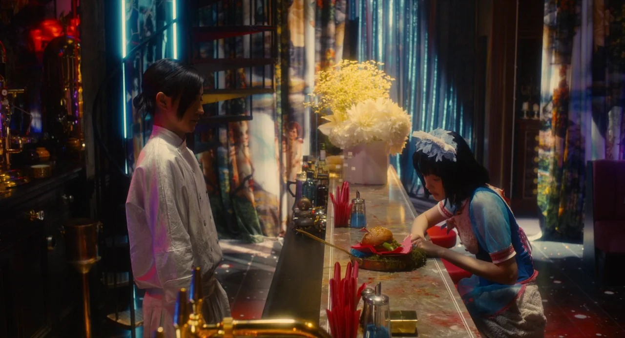 Diner (2019) movie still: medium — A dimly lit restaurant bar features vibrant floral curtains and ornate, colorful decor details. A chef stands…