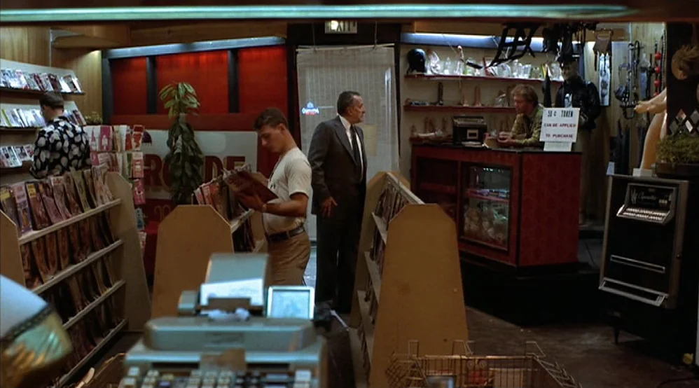 Hardcore (1979) movie still: wide — A cluttered adult bookstore with wooden shelving units displaying magazines and various adult merchandise. A man…