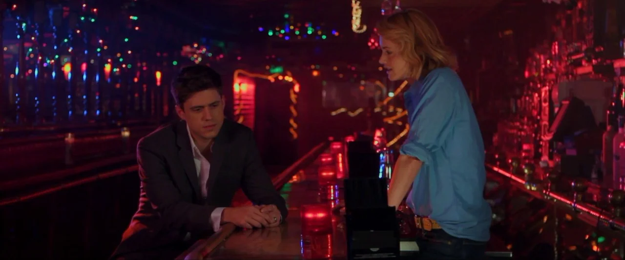 Girl Walks Into a Bar (2011) movie still: medium — A dimly lit bar at night features colorful decorative lights reflected on polished surfaces. A…