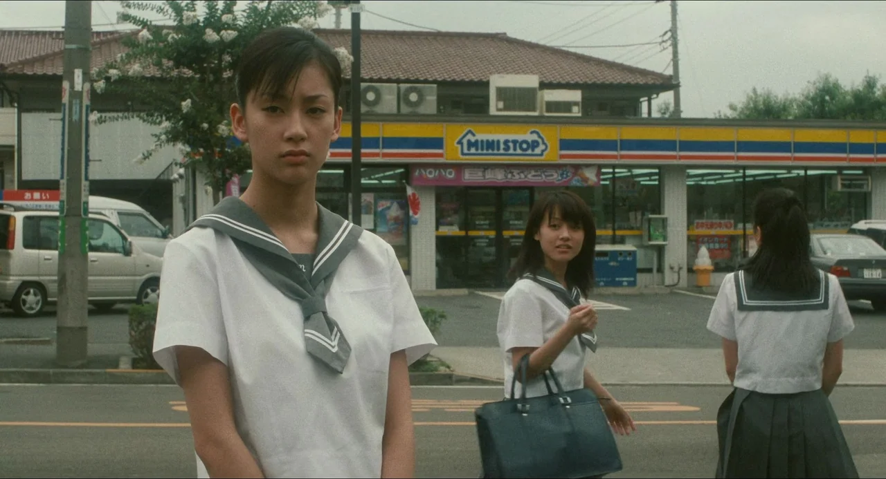 Dark Water (2002) movie still: medium — A Japanese convenience store parking lot with a yellow and blue signage facade. Three school-aged girls in…