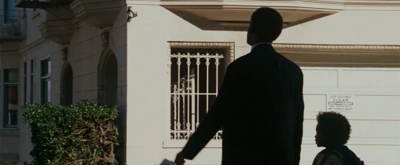The Pursuit of Happyness (2006) movie still: medium — A man and a child stand on a light-colored urban residential street. The pair gazes upward…