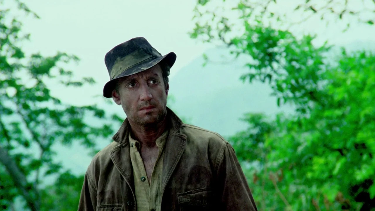 Sorcerer (1977) movie still: medium — A man stands in a dense, humid jungle environment with blurred green trees surrounding him. The subject looks…