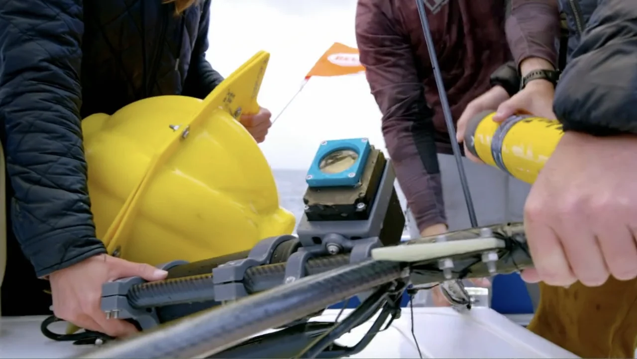 Alien Sharks: Strange New Worlds (2023) movie still: medium — An open boat deck on a cloudy day with an orange research flag visible. Two people…