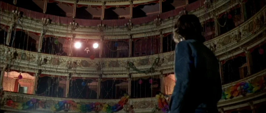 Four Flies On Grey Velvet (1971) movie still: medium — A dimly lit, ornate opera house interior with tiered balconies adorned with festive garlands.…