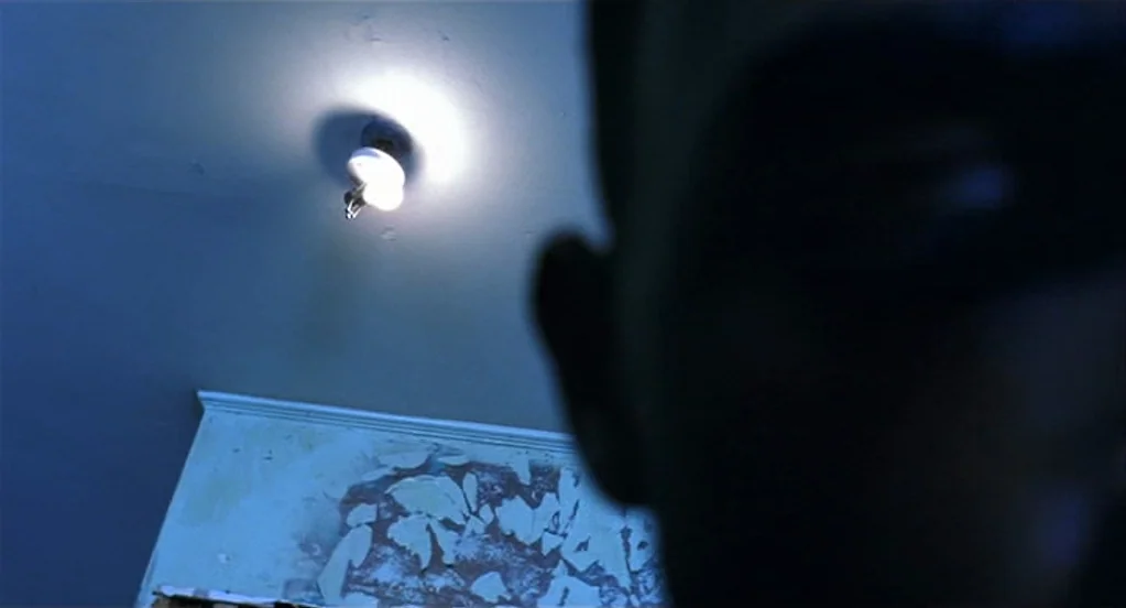 Traffic (2000) movie still: closeup — A room with a blue-toned ceiling and a section of wall with peeling paint. A man stands in the extreme…