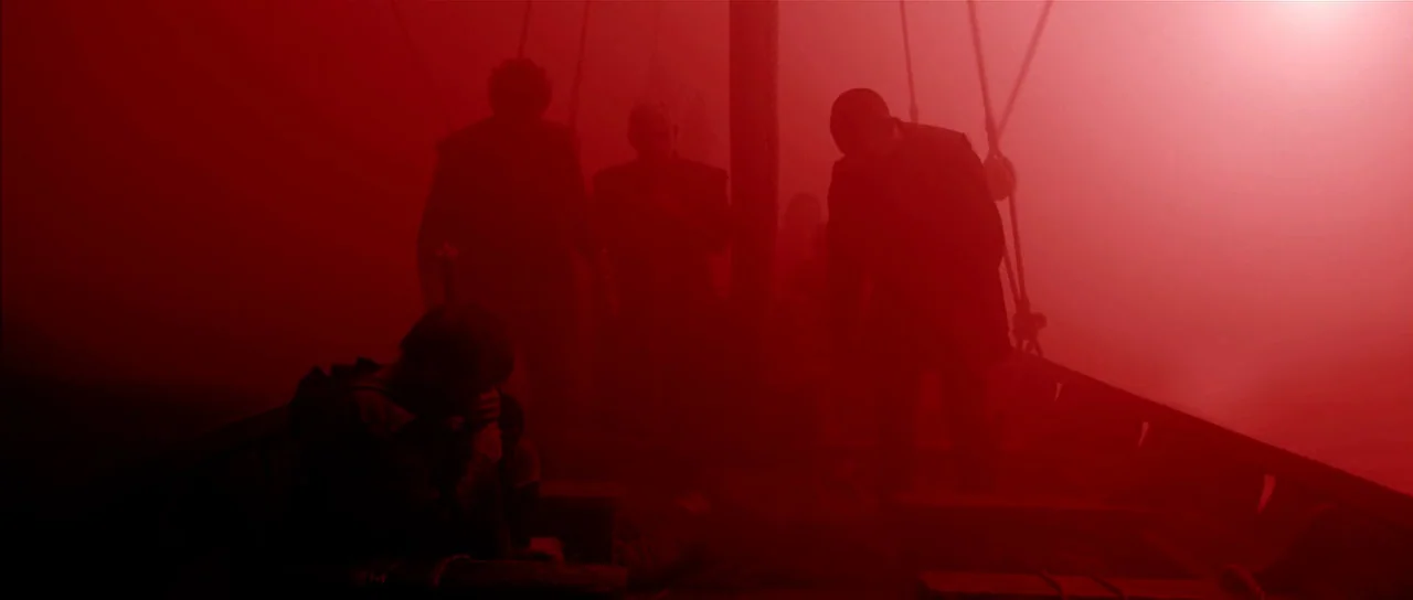 Valhalla Rising (2009) movie still: wide — A boat deck is saturated in an intense, pervasive red light. Silhouetted figures stand and sit on the…