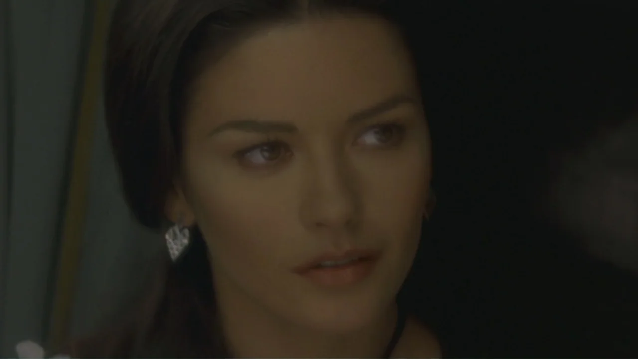 The Mask of Zorro (1998) movie still: closeup — A woman stands in a dimly lit indoor space with blurred dark shadows behind her. She looks to the…