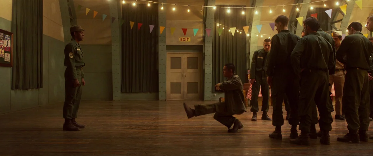 Swing Kids (2018) movie still: wide — A spacious hall features a wooden floor, decorative pennant flags, and an exit sign. One soldier performs a…