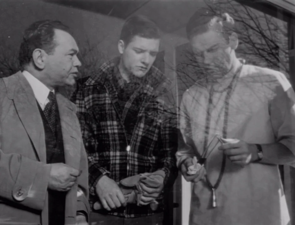 The Stranger (1946) movie still: medium — An interior sunroom features a glass door with visible reflections of bare tree branches. Three men in…
