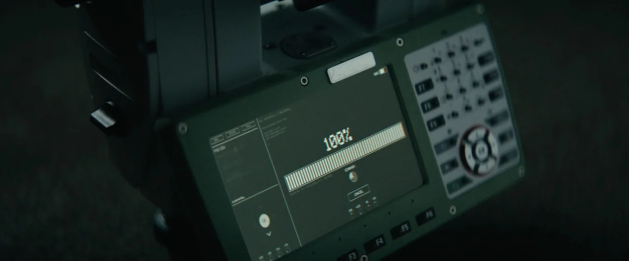 The Vault (2021) movie still: closeup — A dark digital interface shows a progress bar reaching its completion percentage. The device casing is dark…