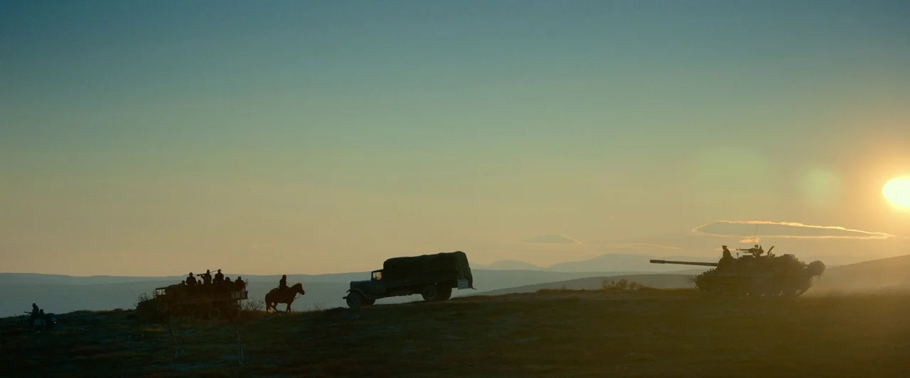 Sisu (2022) movie still: wide — A military convoy consisting of a truck and a tank travels along a ridge. A rider on horseback accompanies the…