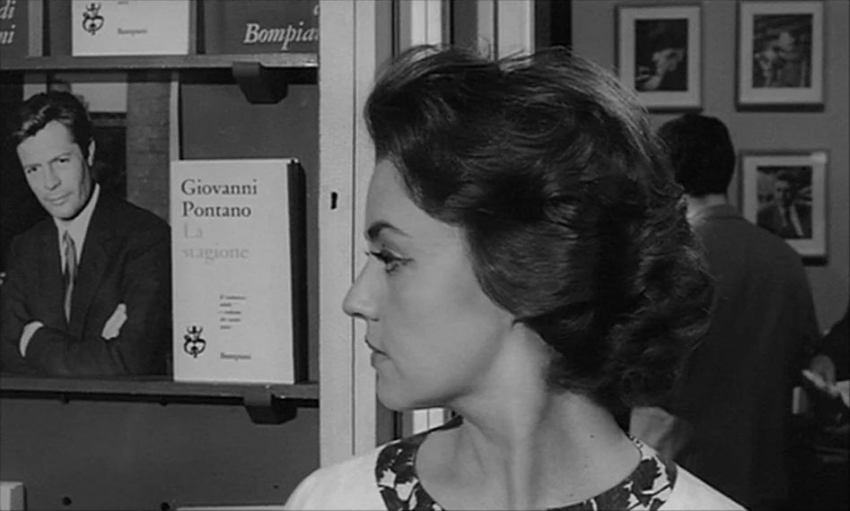 La Notte (1961) movie still: closeup — A well-lit bookstore interior features bookshelves lined with various titles and framed pictures. A woman in…
