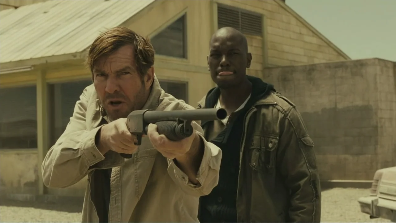 Legion (2010) movie still: medium — A dusty outdoor lot features a light-colored building with a triangular roof. A man in a tan jacket holds a…