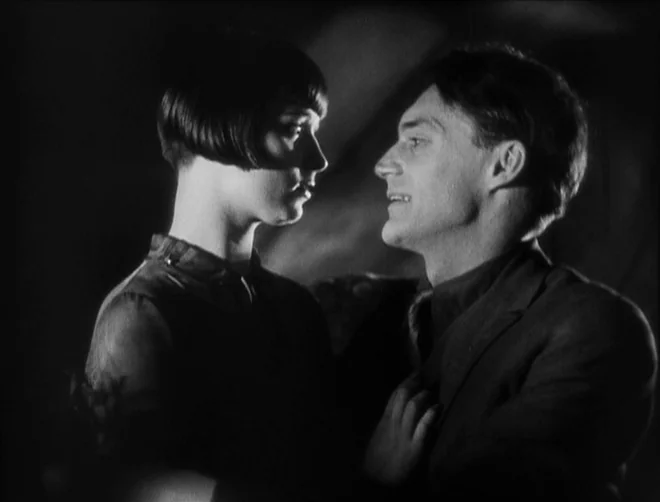 Pandora’s Box (1929) movie still: medium — A dimly lit interior space is visible only through high-contrast black and white tones. A young woman and…