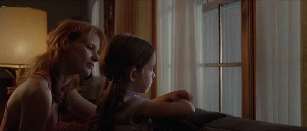 Take Shelter (2011) movie still: medium — A domestic interior with a large window draped in sheer white curtains. A woman in a pink top gently…