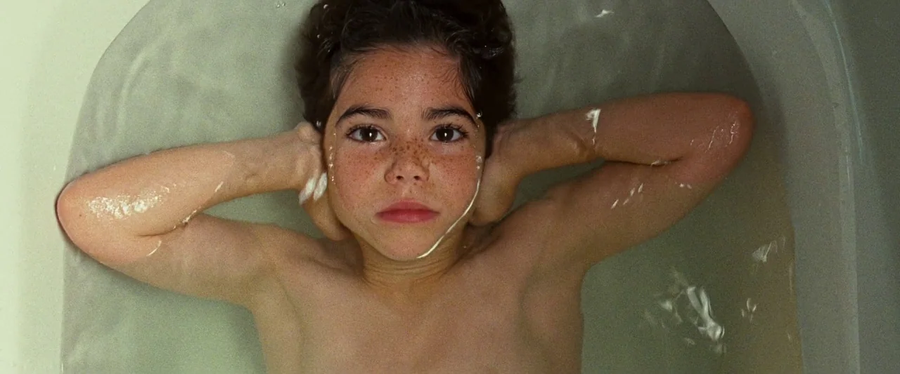 Mirrors (2008) movie still: closeup — A white ceramic bathtub is filled with shallow, clear water. A young boy lies submerged to his shoulders,…