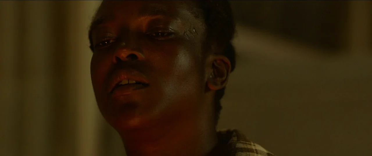 His House (2020) movie still: closeup — A dark indoor space where the person is bathed in warm, directional light. The subject is gazing toward the…